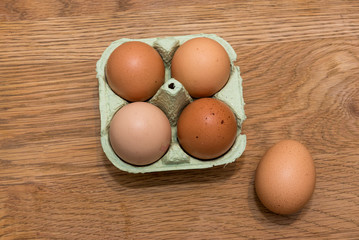 Close-up view of raw chicken eggs in egg box on  oak wooden background