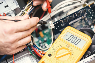 Technician hands with voltmeter above computer motherboard. Repair of computers concept. Toned with selective focus - obrazy, fototapety, plakaty