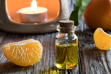 A bottle of tangerine essential oil with fresh tangerines and an aroma lamp