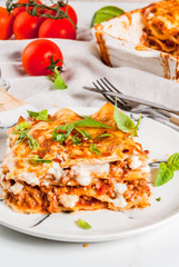 Italian food recipe. Dinner with classic lasagna bolognese with béchamel sauce, parmesan cheese, basil and tomatoes, on white marble table, coopy space