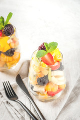 Vegan dietary foods. Vitamins. Dessert. Summer. Salad of fresh organic fruits - mango, peach, apple, banana, kiwi, strawberry, blackberries. In a serving glass. On a white concrete table. copy space