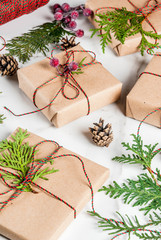 Christmas gift or present box wrapped in kraft paper, decorated with christmas tree branches, pine cones, red berries, on white marble table, copy space