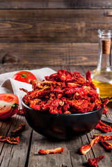 Homemade sun-dried organic tomatoes, crispy tomato chips, on an old rustic wooden table with fresh tomatoes and olive oil. Copy space