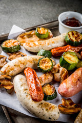 Barbecue. Assortment of various grilled meat sausages, with vegetables BBQ - mushrooms, tomatoes, zucchini, onions. On a black stone table, on a baking sheet, with sauce. Copy space