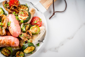 Barbecue. Assortment of various grilled meat sausages, with vegetables BBQ - mushrooms, tomatoes, zucchini, onions. On white marble table, on plate, with sauce. Copy space top view