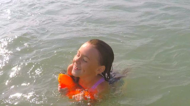 A happy child is swimming in the sea. A little girl is swimming in a pond.