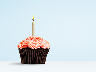 Pink cupcake with candle flame on blue background