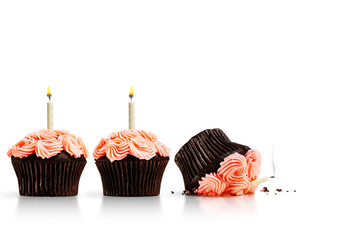 Accident, dropped cupcake in row of pink cupcakes with candles isolated on white