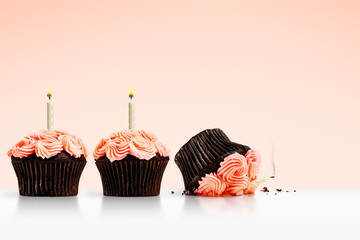 Smashed cupcake in row of cupcakes with candles on pink background