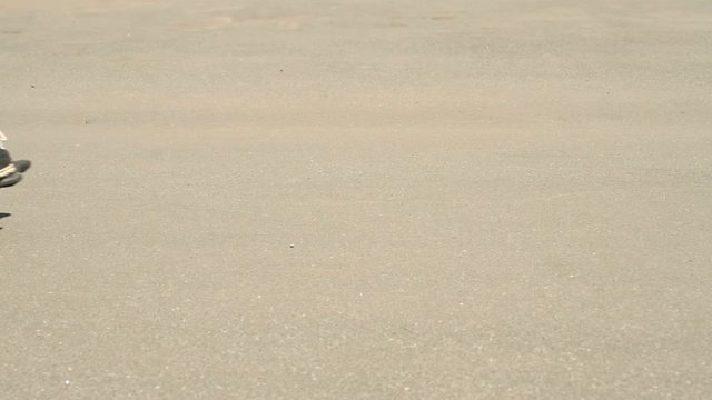 Close-up of feet of skateboarder boy on skateboard passing along road in sunlight in summer season