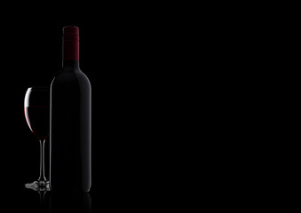 Glass of red wine with bottle with shape on black