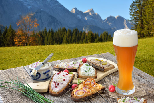 Brotzeit mit einem Hefeweißbier rustikal in den bayerischen Alpen serviert -  Hearty snack with a yeast wheat beer served in the Bavarian Alps 