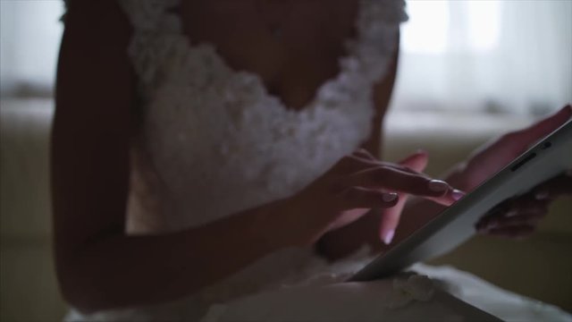 Woman using tablet computer touch screen on a modern sofa in a dining room. Lateral view, slightly flare from the window, blue technological cast and tilt-shift lens used 4k ursa mini 4,6k