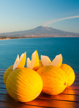 Typical mediterranean fruits: yellow melon with blue sea and Mount etna in the background