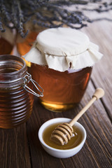 Honey dripping from a wooden honey dipper in a jar on wooden background