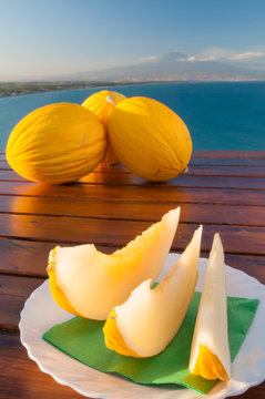 Typical mediterranean fruits: yellow melon with blue sea and Mount etna in the background