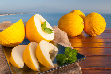 Typical mediterranean fruits: yellow melon with blue sea and Mount etna in the background