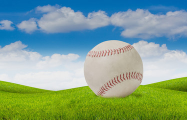 old white baseball on grass and blue sky background.