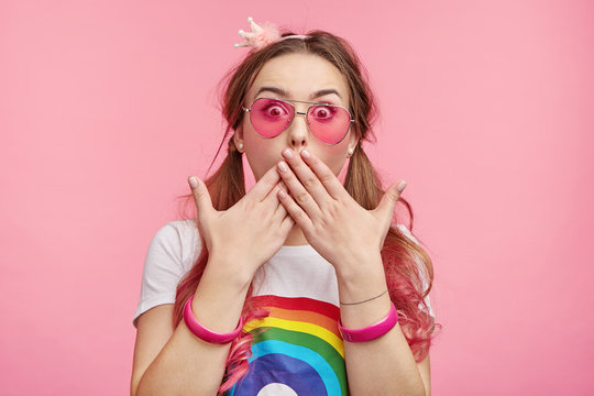 Indoor picture of shocked female lady stares with bugged eyes, covers mouth with hands as tries to control emotions and not screm loudly in surprisment, sees awful car accident on her own eyes
