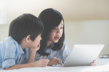 Obraz premium Asian children lying in bed and using laptop
