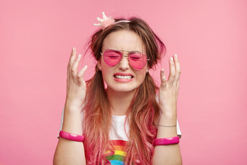 Emotional desperate dejected coquette woman finds out that she loose beauty contest, can`t control negative emotions, has sad and depressed expression, clenches teeth and gestures over pink wall