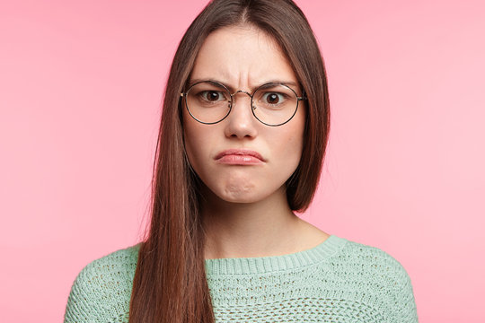 Aggravated brunette female with long straight dark hair, wears spectacles, frowns face in discontent, feels displeasure, being insult by someone. Headshot of Asian woman has annoyed expression