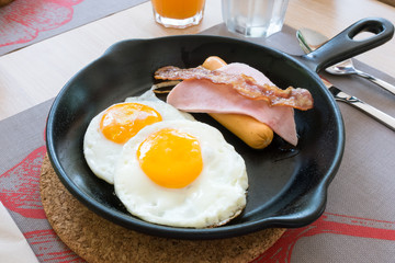 Fried egg with, sausage, ham, and bacon pieces in iron frying pan
