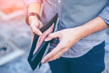 Man standing holding black wallet full of money