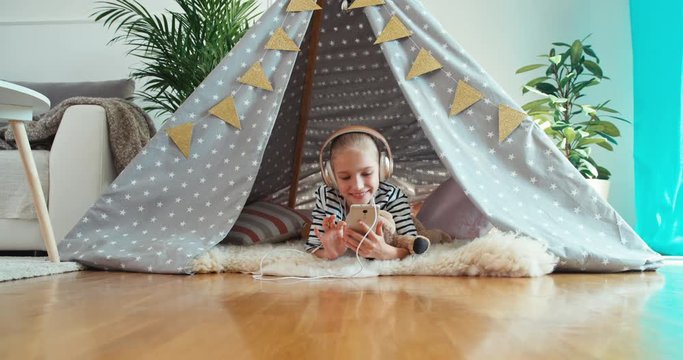 Girl using cell phone listening music in headphones and smiling at camera