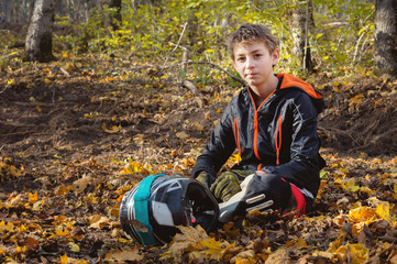 Portrait of a young rider mtb sitting in the forest on a yellow foliage holding a full-face helmet