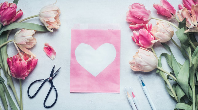 Lovely pastel color spring mock up with tulips, scissors , markers and pink pack paper bag  with heart , top view, flat lay