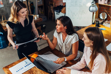 Group of creative female designers working on a new project together talking, discussing, suggesting ideas sitting in contemporary studio