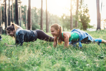 Two girlfriends working out outdoors doing plank exercise on grass