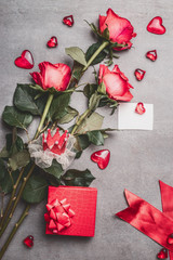 Valentines day, love or dating concept. Red roses bunch with gift box, blank paper greeting card, ribbon and hearts , top view, mock up