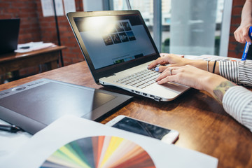 Close-up view of interior designer workspace with laptop, graphic tablet, phone and color palette...