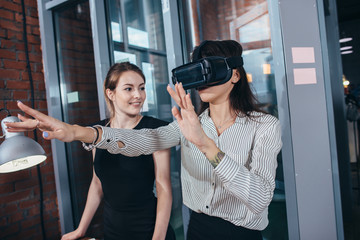 Naklejka na ściany i meble Female office workers having fun at work watching 3d video in VR goggles, woman touching something experiencing virtual reality