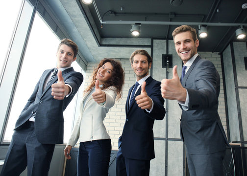 Portrait of happy businesspeople standing in office showing thumb up.