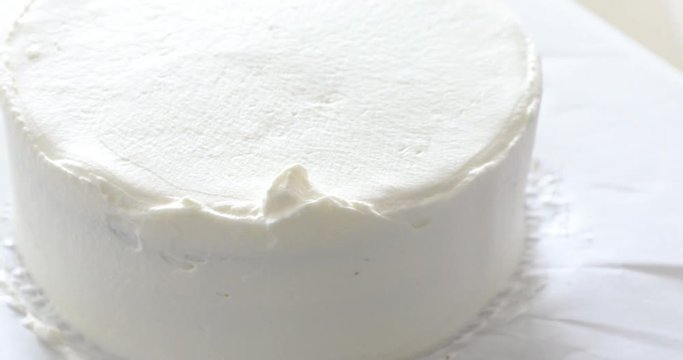 Woman's hand spreading whipped white cream on chocolate sponge cake