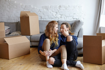 Candid shot of beautiful stylish young couple in love having fun in their new apartment, feeling happy and excited about moving in together, sitting on floor and relaxing after cleaning and unpacking