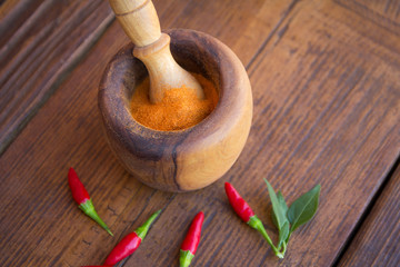 Hot chili powder in the bowl. In addition to the bowl on the wooden background, hot chilli peppers