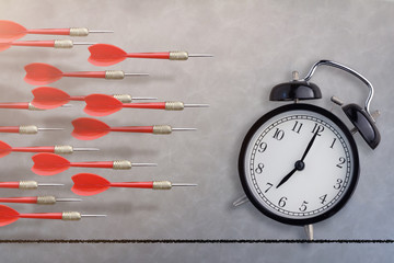 black alarm clock and red dart arrow fly on  gray leather texture floor background free copyspace...