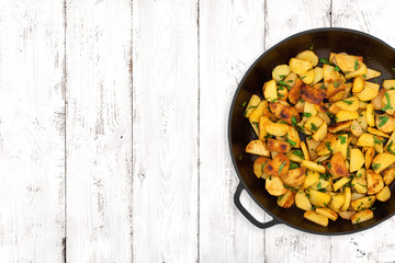 Fried potatoes in a cast iron pan on light wooden background, top view