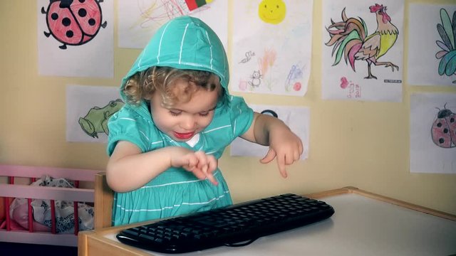 Funny lovely child girl typing computer keyboard and looking at camera and smile