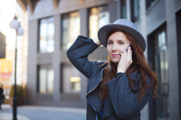 Outdoor portrait. Young stylish beautiful woman in hat speaking on phone while walking in the big city streets. 