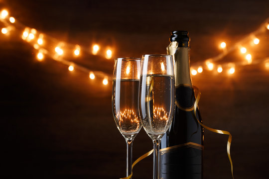 Festive photo of two wine glasses with wine, bottles, cork, burning garland