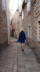 Fototapeta premium Девушка в шляпе идет по старинному городу Будва в Черногории
