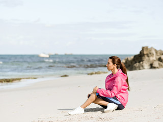 Fototapeta na wymiar Young woman sitting at the beach in sportswear