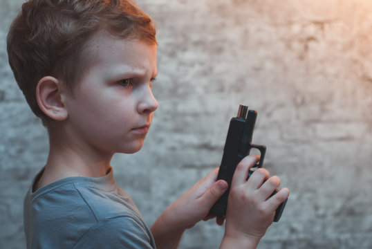 Boy with gun in hand against a brick wall,