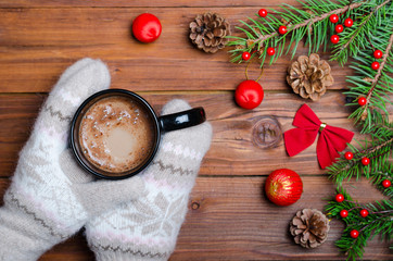 Women's hands in mittens holding a cup of hot drink on a wooden table top view.