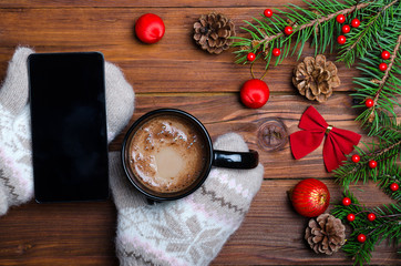 Female hands holding a cup with a hot drink and a smartphone over a wooden table top view.